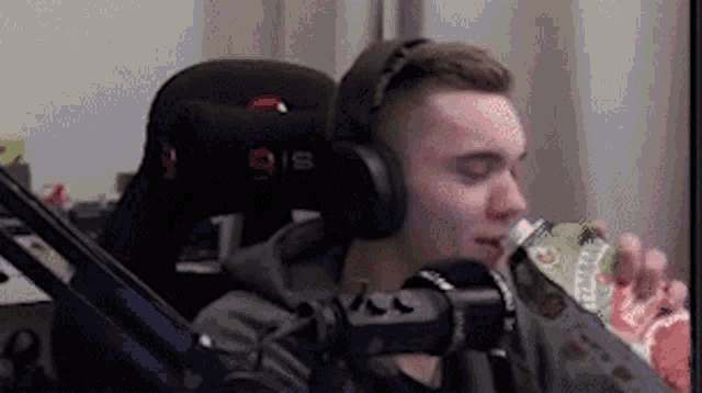 a man wearing headphones is sitting in front of a microphone drinking a bottle of soda .