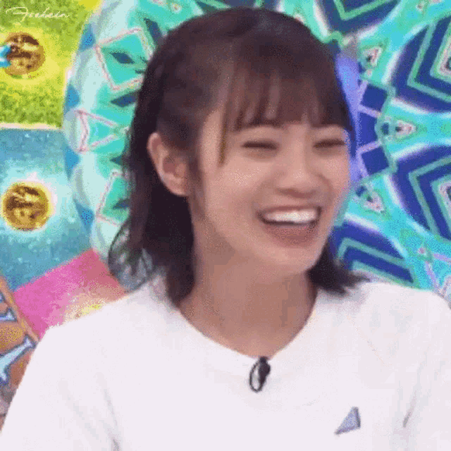 a woman is smiling with her eyes closed and wearing a white shirt with a microphone .