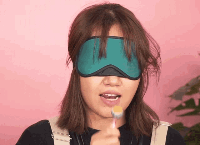 a woman wearing a blindfold brushes her teeth