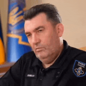 a man in a police uniform is sitting at a desk in front of a flag .
