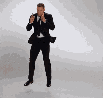 a man in a suit and tie is dancing in front of a white wall