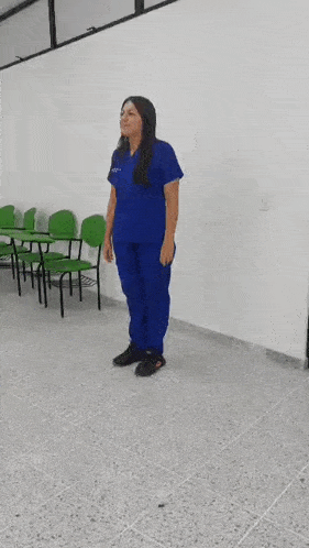 a woman in a blue scrub suit is walking in a classroom with green chairs .