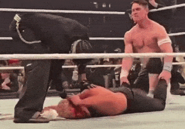 a wrestler is laying on the ground in a wrestling ring with blood on his face .