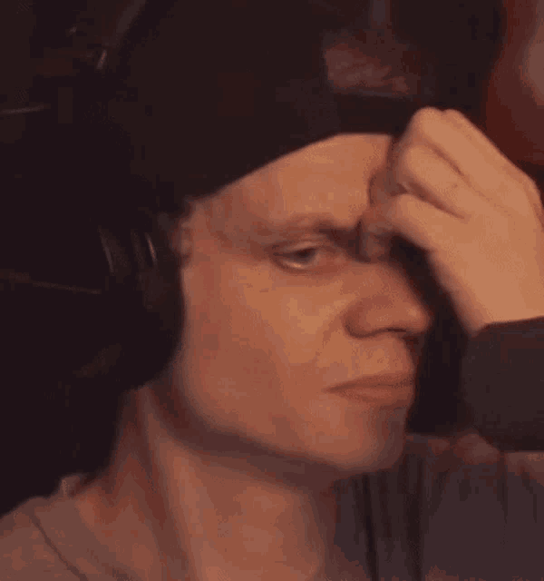 a man wearing headphones and a beanie is scratching his forehead .