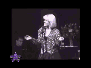 a woman singing into a microphone with a star that says jamie de roy & friends