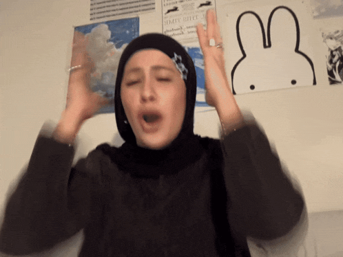 a woman wearing a hijab is making a funny face in front of a picture of a rabbit