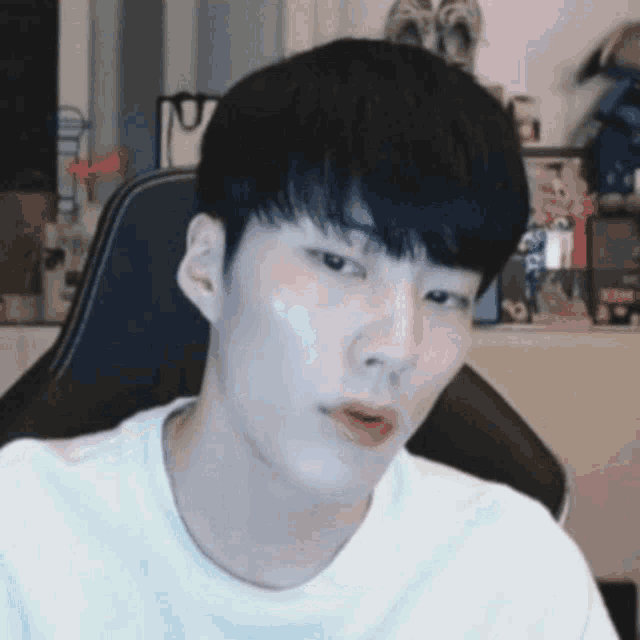 a young man in a white shirt is sitting in a chair and making a funny face .