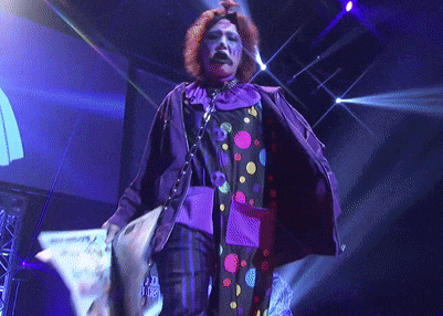 a man in a clown costume is holding a piece of paper that says ' a ' on it