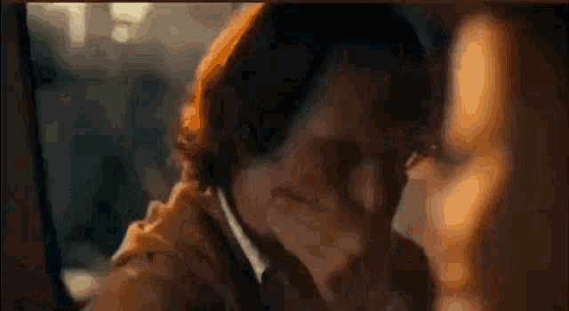 the joker is covering his mouth with his hand in a close up of a movie scene .