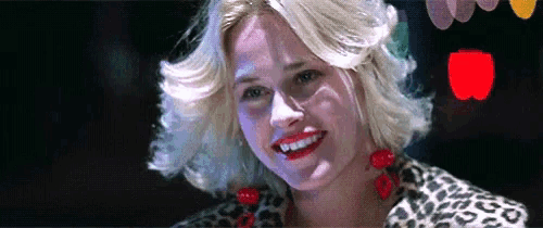 the woman is wearing a leopard print jacket and red earrings .