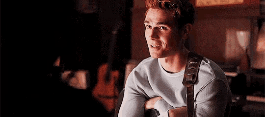 a man is sitting in a chair with his arms crossed and a guitar strap around his neck .