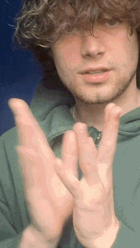 a young man wearing a green hoodie is clapping his hands together