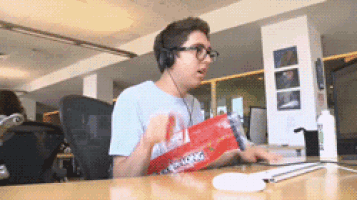a man wearing headphones is sitting at a desk holding a bag of crunchy peanut butter