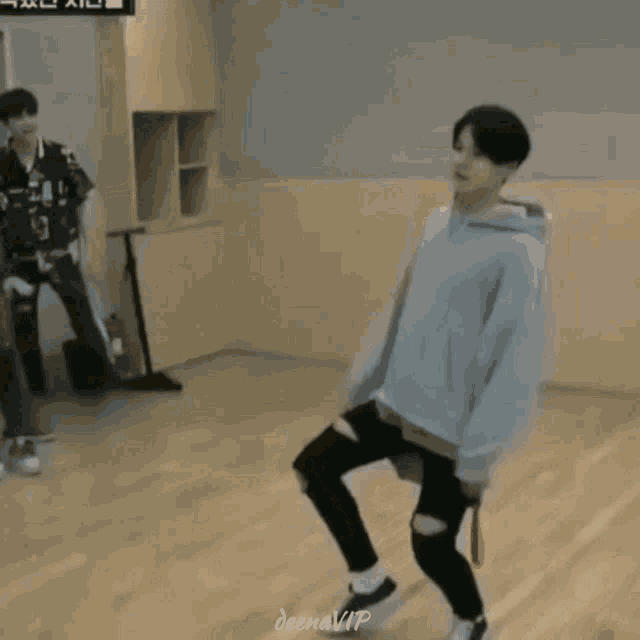 a man in a grey hoodie is dancing on a wooden floor while another man looks on .