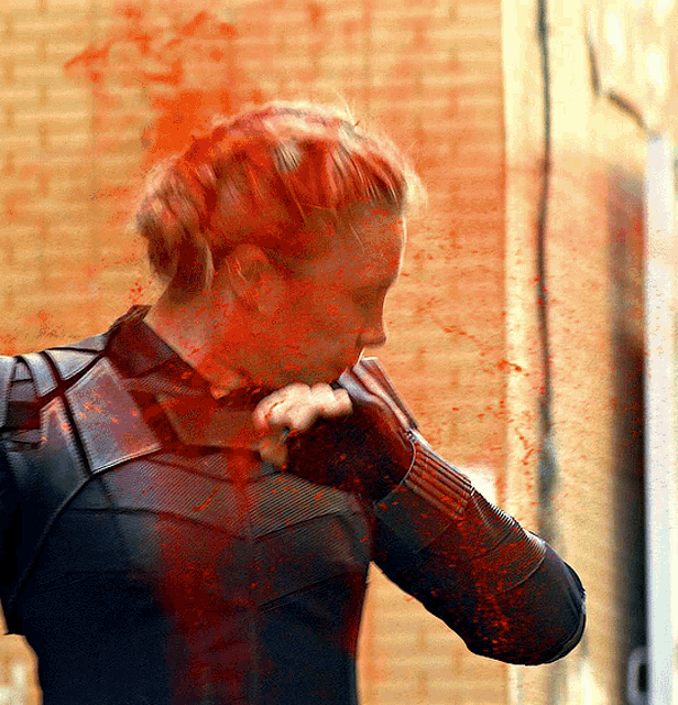 a woman with red hair is standing in front of a brick wall