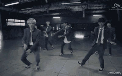 a group of young men in suits and ties are dancing together in a dark room .
