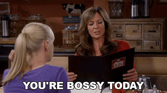 two women are sitting at a table and one of them is holding a menu and the other is saying " you 're bossy today "
