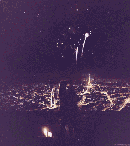 a couple kissing in front of a fireworks display with a candle in the foreground