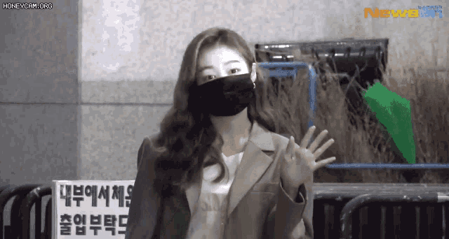 a woman wearing a mask is waving her hand in front of a sign that says newsen .