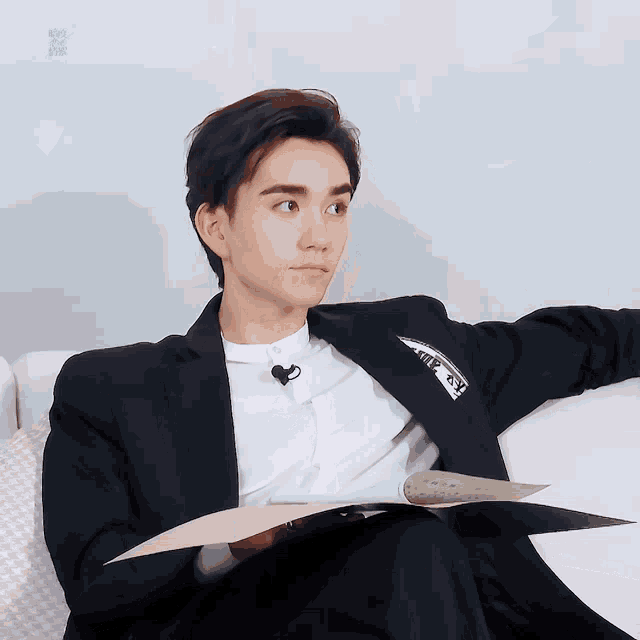 a man in a suit is sitting on a couch holding a book