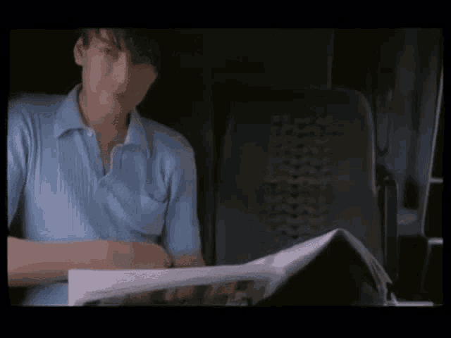 a man in a blue shirt is sitting in a chair reading a magazine .