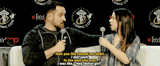 a man and a woman are talking in front of a sign that says emerald city comic con