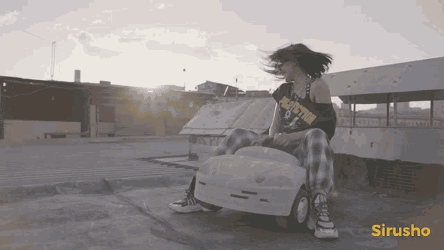 a woman wearing a black shirt that says pulp fiction sits on a small car