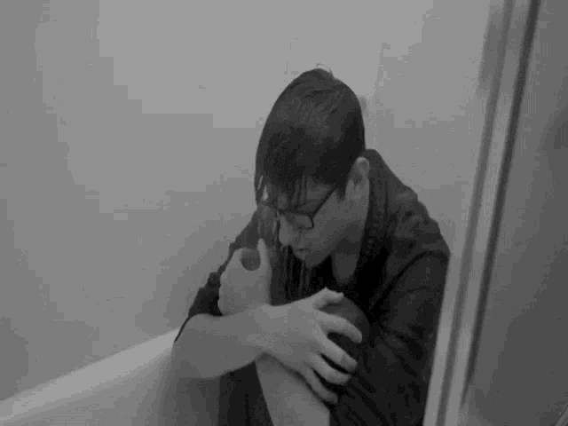 a black and white photo of a man sitting in a bathtub with water running down his face .