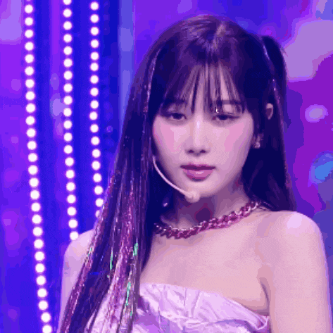 a woman wearing a purple dress and a necklace is standing in front of purple lights