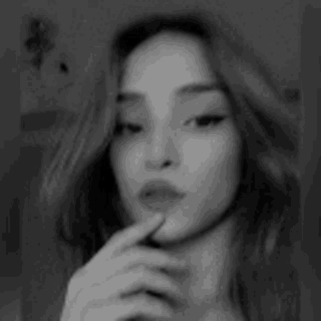 a black and white photo of a woman taking a selfie with her finger to her mouth .