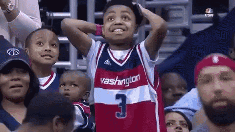a young boy wearing a washington jersey is standing in the stands watching a basketball game .