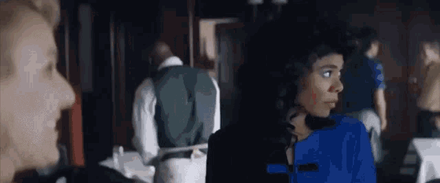 a woman in a blue dress is talking to a man in a green vest .