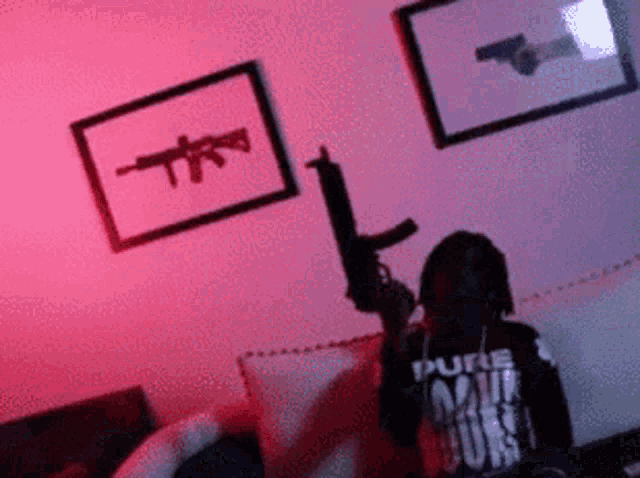a man holding a gun in a living room with a picture of a gun on the wall behind him