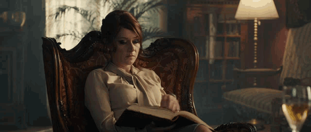 a woman sits in a chair reading a book with a lamp in the background