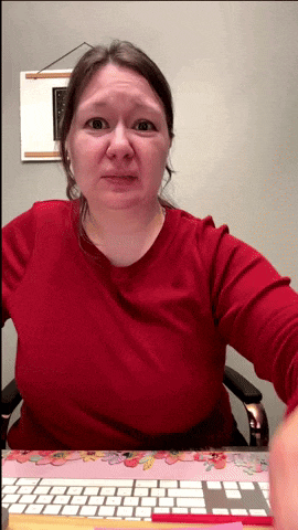 a woman in a red shirt sits at a desk in front of a keyboard