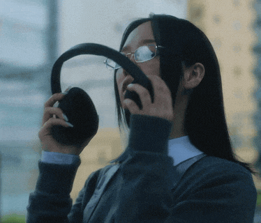 a woman wearing glasses and a gray sweater holds a steering wheel in front of her face