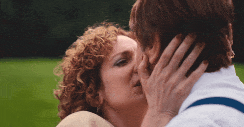a man and woman kissing in a field with the man covering his face