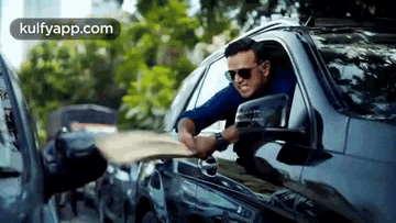 a man wearing sunglasses is sitting in a car holding a piece of paper .
