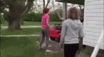 two women are walking in a yard with a red car in the background