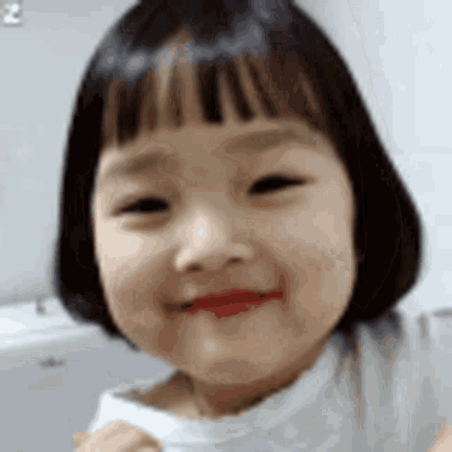 a little girl with short hair and a white shirt is smiling .