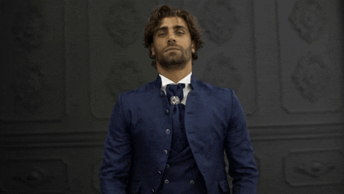 a man in a blue suit and tie stands in front of a wall