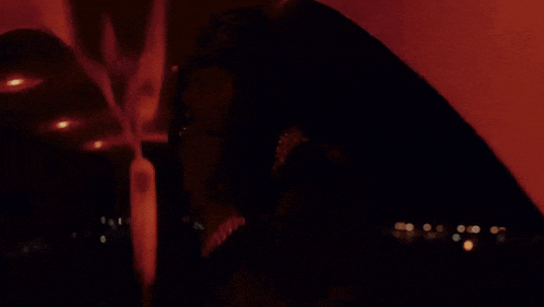 a woman is smoking a cigarette in a dark room with a red light behind her .