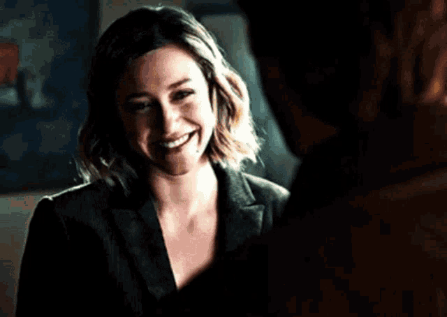a woman in a suit is smiling while looking at a man in a dark room .