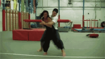 a man and a woman are wrestling in a gym and the man is holding the woman 's head