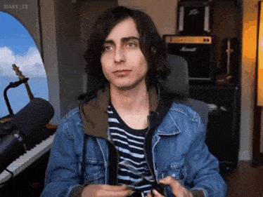 a young man wearing a denim jacket is sitting in front of a microphone