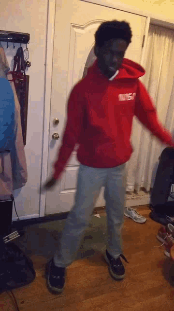 a man in a red hoodie is dancing in front of a door .