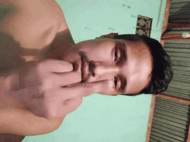a shirtless man with a beard holds his fingers to his mouth