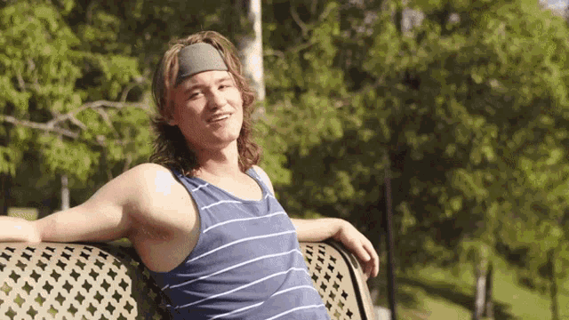 a man wearing a headband sits on a bench in the park