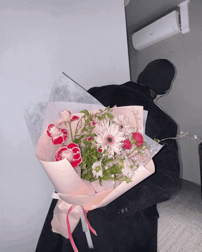 a person holding a bouquet of pink flowers in front of a wall