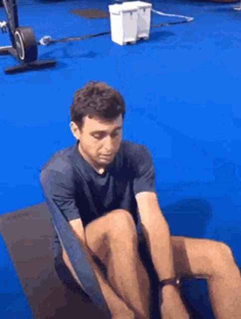 a man is sitting on a yoga mat on a blue floor .